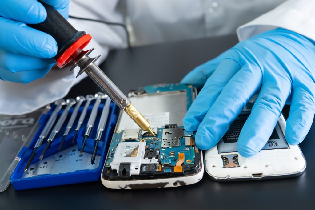 Technician repairing inside of mobile phone by soldering iron.