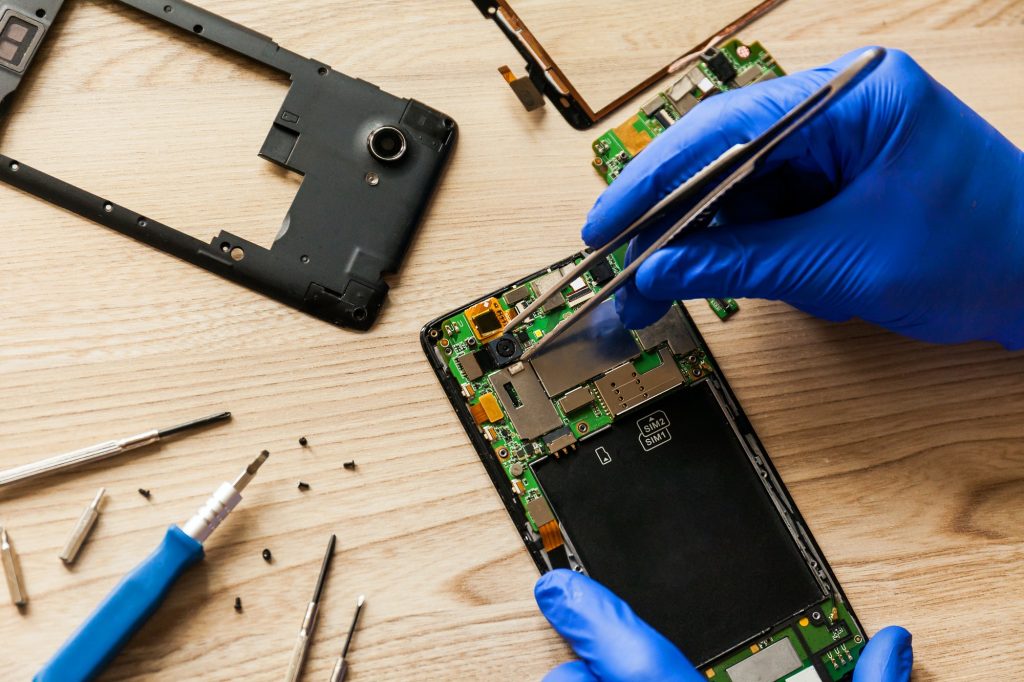 The technician repairing the smartphone's motherboard in the workshop on the table.