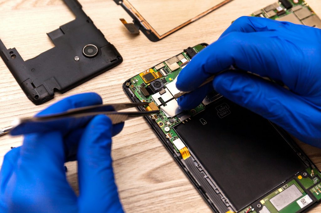 The technician repairing the smartphone's motherboard in the workshop on the table.